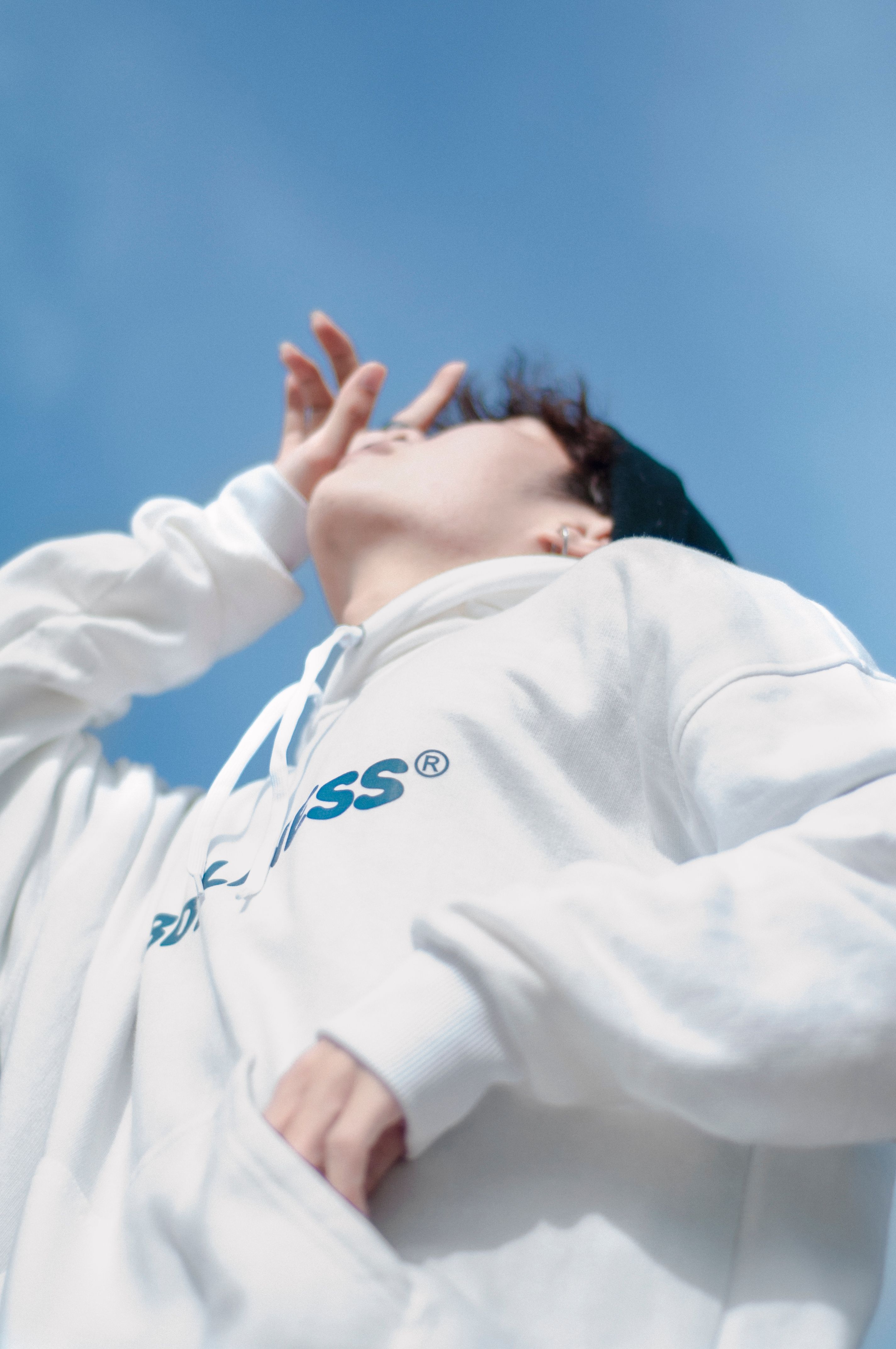 Portrait of a young adult in a white hoodie, gazing at the sky.