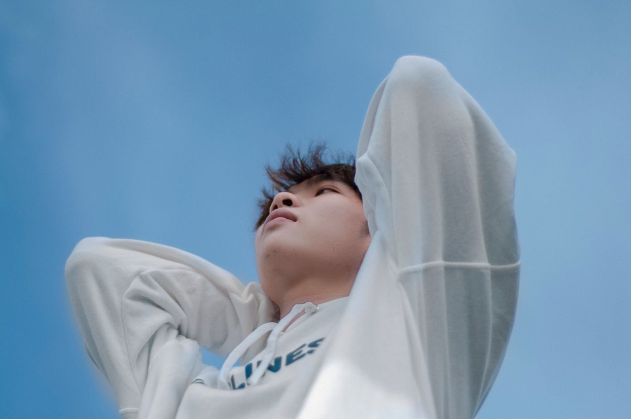 young man in a white hoodie gazing up contemplatively against a clear