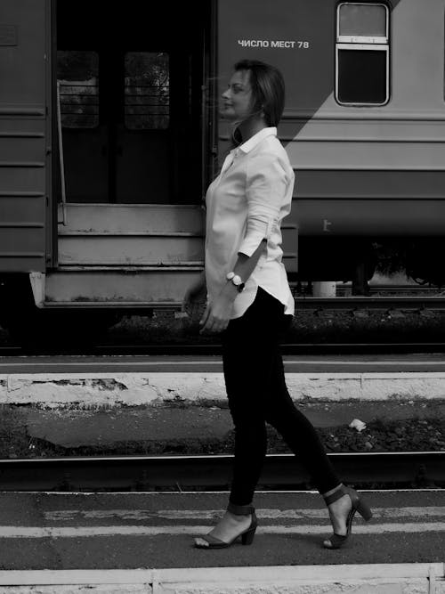 Free Woman in White Dress Shirt and Black Pants Standing beside a Train  Stock Photo