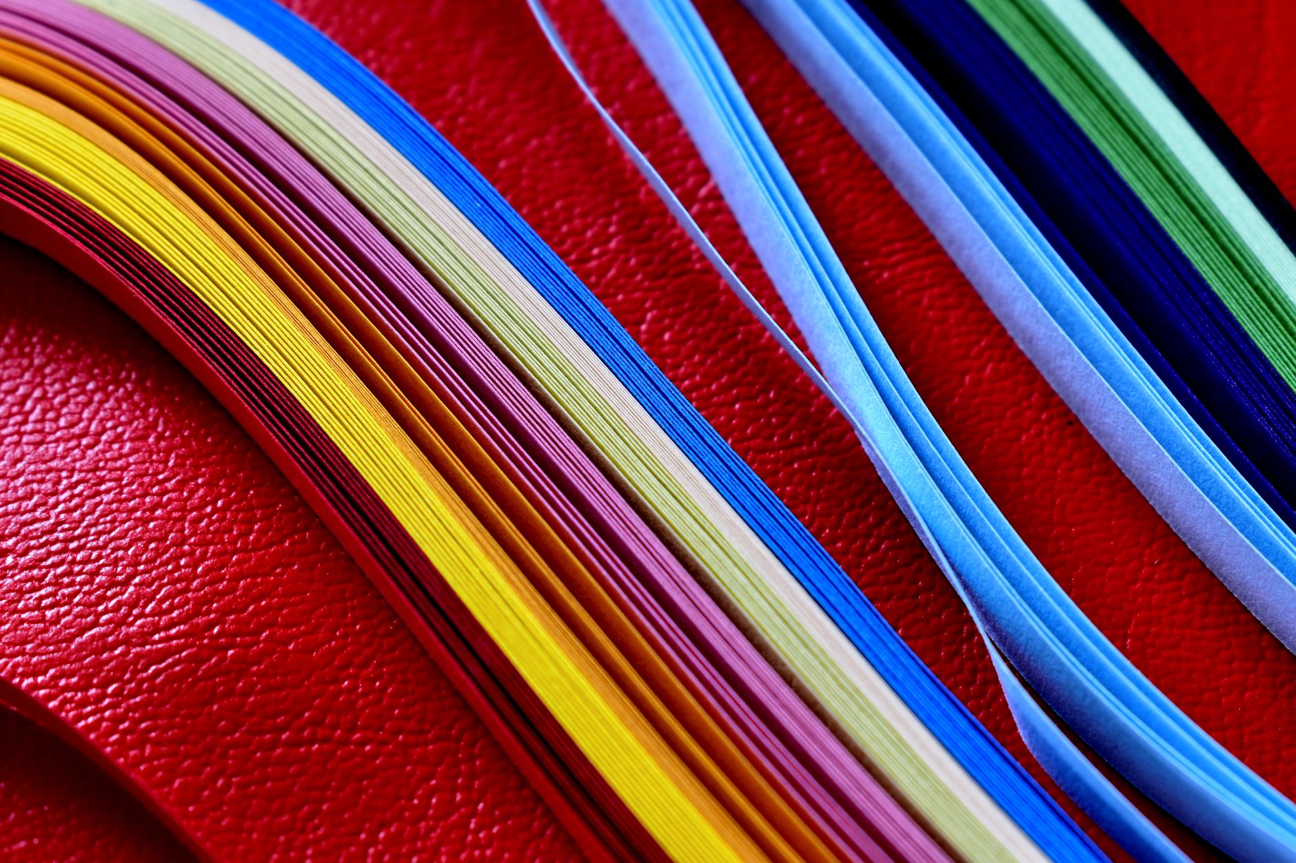 Vibrant strips of colored paper on a red textured background, perfect for craft projects.