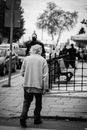 Grayscale Photo of Woman in White Coat and Black Pants Standing on Sidewalk
