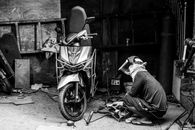 Welder repairing a motorcycle in a workshop, captured in black and white.