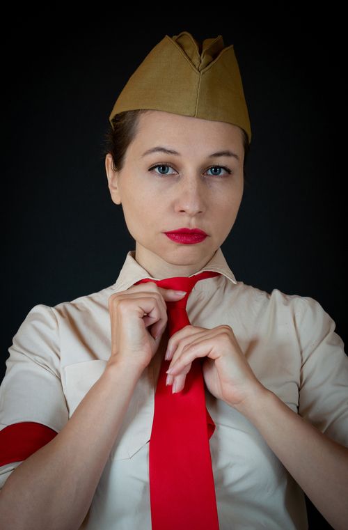 Free Close-up portrait of a woman in a historical military uniform adjusting a red tie with a garrison cap. Stock Photo