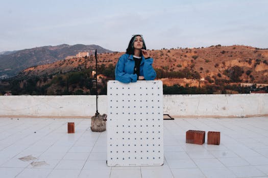 A fashionable woman poses on a rooftop with a stunning view of hills at sunset.