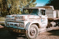 一辆年久生锈的卡车停在户外，阳光明媚，四周绿树环绕