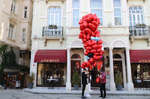 Men Holding Red Balloons in Front of a Coffee Shop