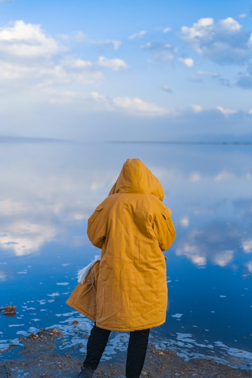Back Footage of a Person in Yellow Hoodie Standing on Seashore