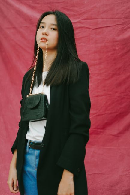 Stylish woman in studio with a chain bag in front of red backdrop.