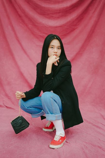 Fashionable young woman crouching with a chic bag in a studio setting with a vibrant pink backdrop.