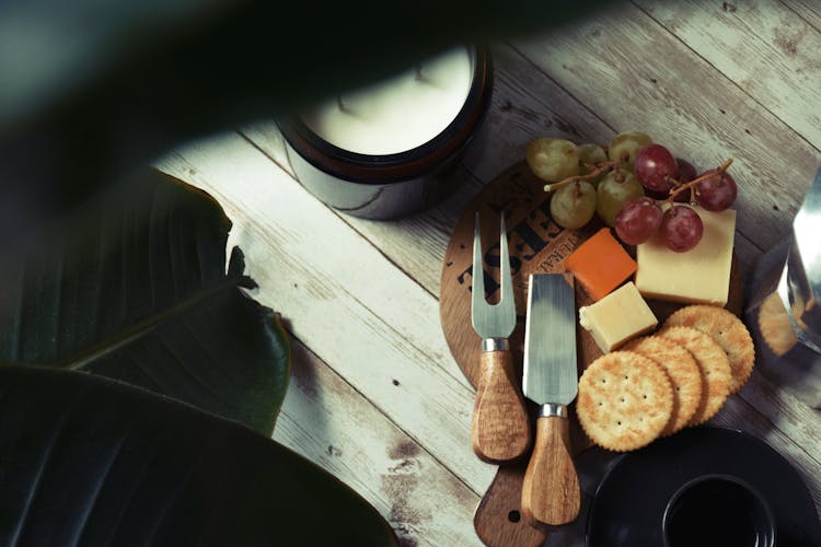 Top View Of A Cutting Board With Cheese, Crackers And Fruit