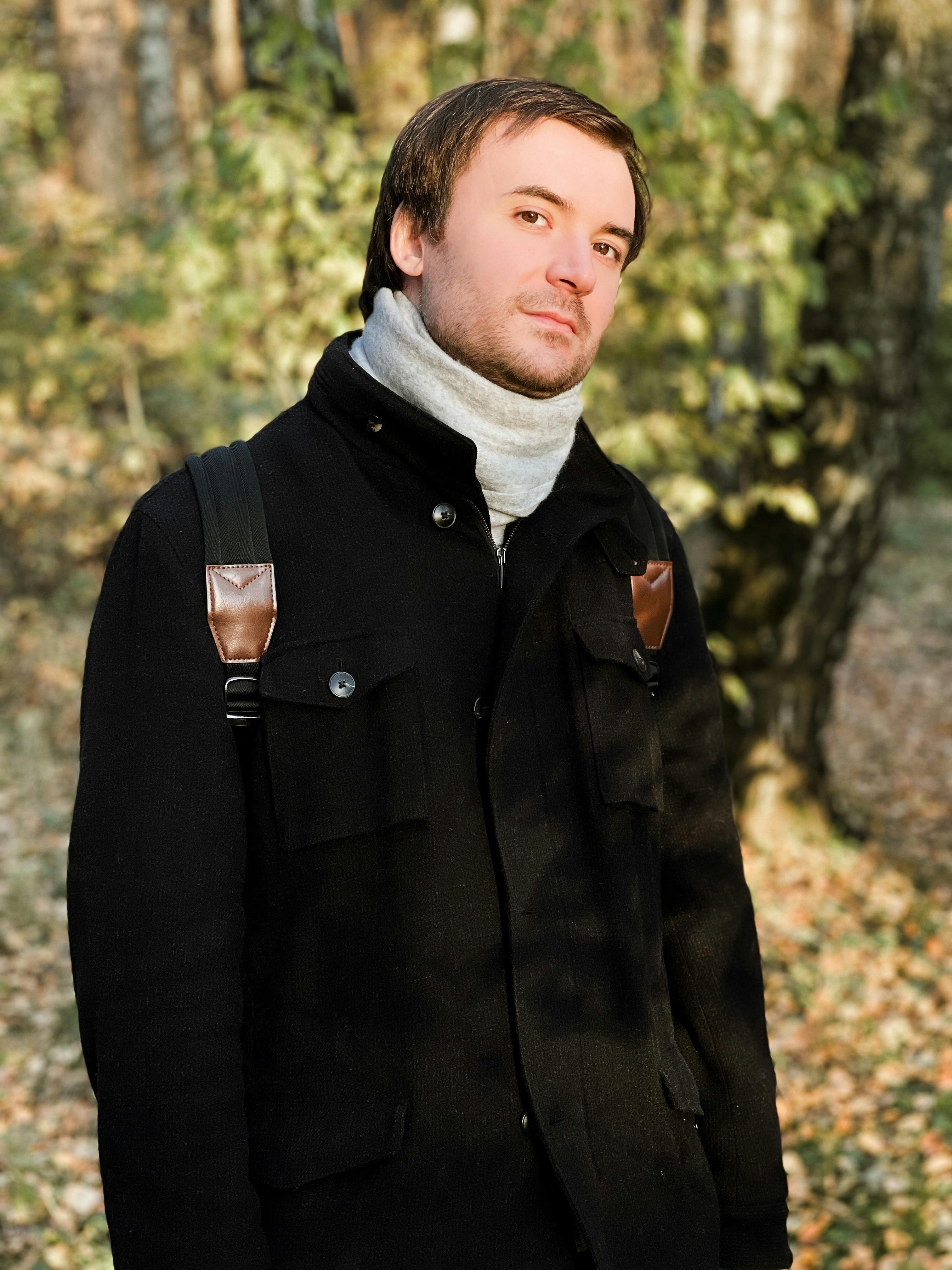 Portrait of a young man wearing a black coat, surrounded by autumn foliage in Russia.