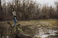 一位女子自信地站在宁静的森林沼泽中的一根原木上，捕捉着秋天宁静的氛围