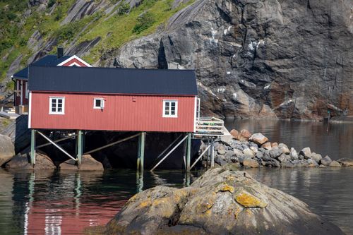 Free Charming red house perched on rocks by a fjord in Flakstad, Norway, under clear skies. Stock Photo