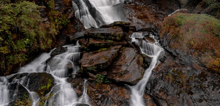 A tranquil waterfall flowing over rocks surrounded by lush greenery in a natural setting.