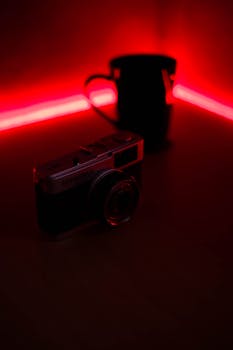 Close-up of a vintage camera illuminated by red neon light on a dark table, creating a dramatic effect.