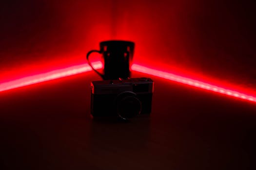 A vintage camera and mug with a striking red LED background create a moody atmosphere.