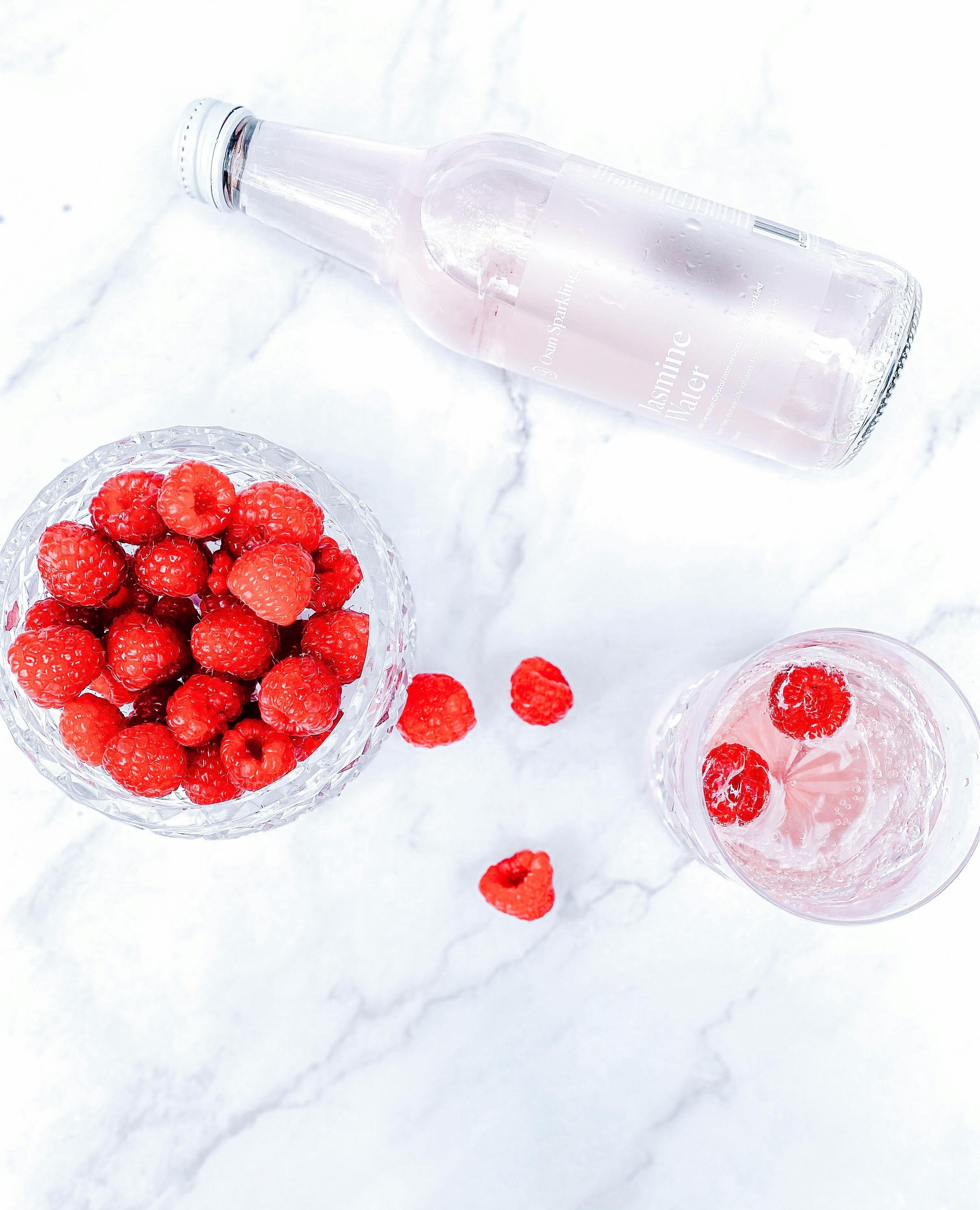 Sparkling raspberry drink in crystal glasses, featuring fresh raspberries and a chilled bottle on marble.