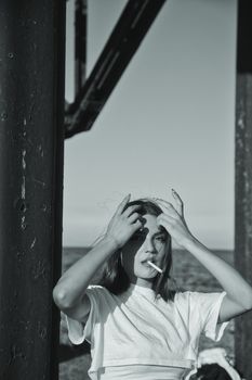 Artistic black and white photo of a woman smoking against an industrial structure by the sea in Cyprus.