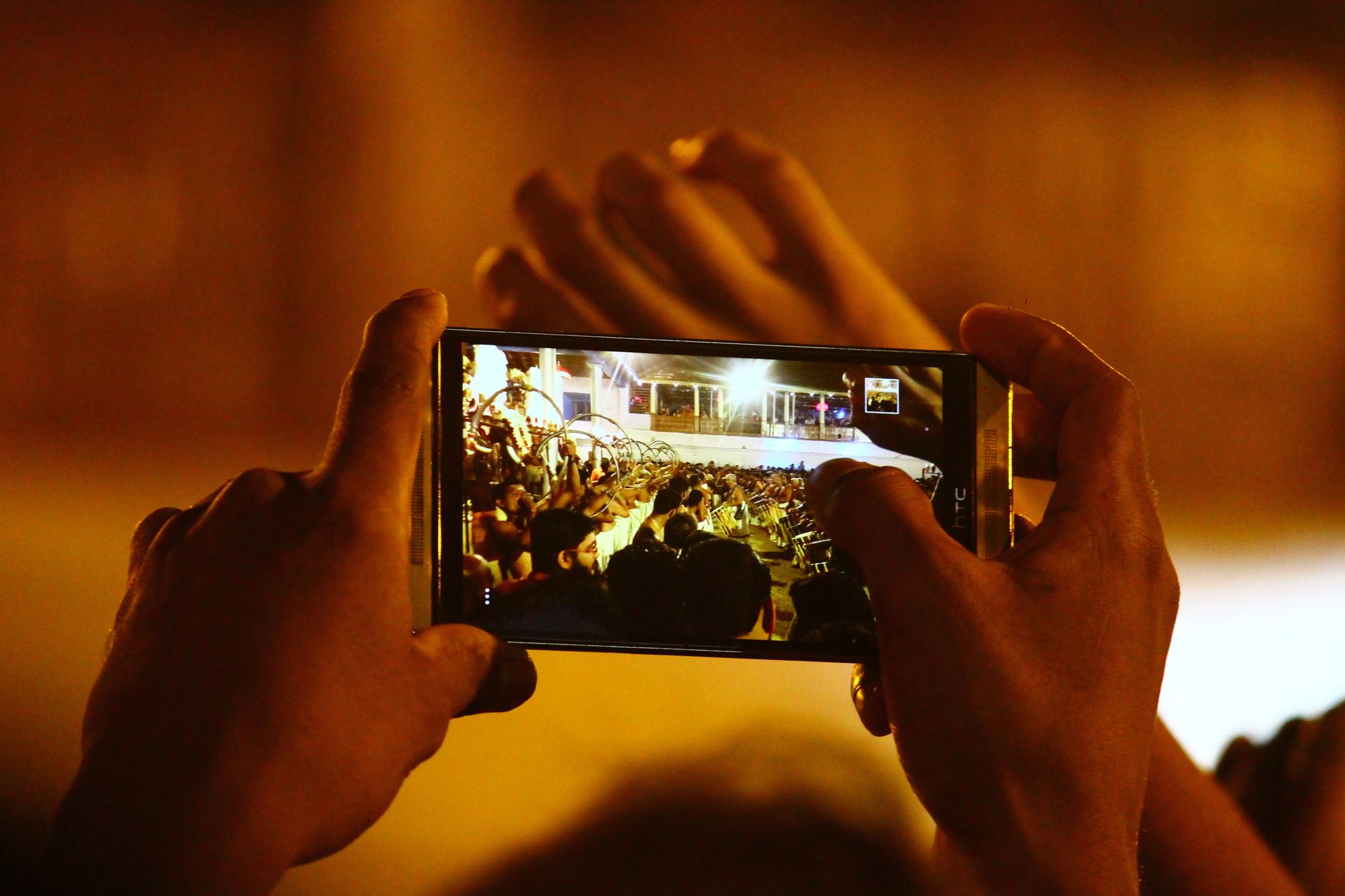 Hands holding a smartphone capturing a live concert scene, highlighting modern tech usage.