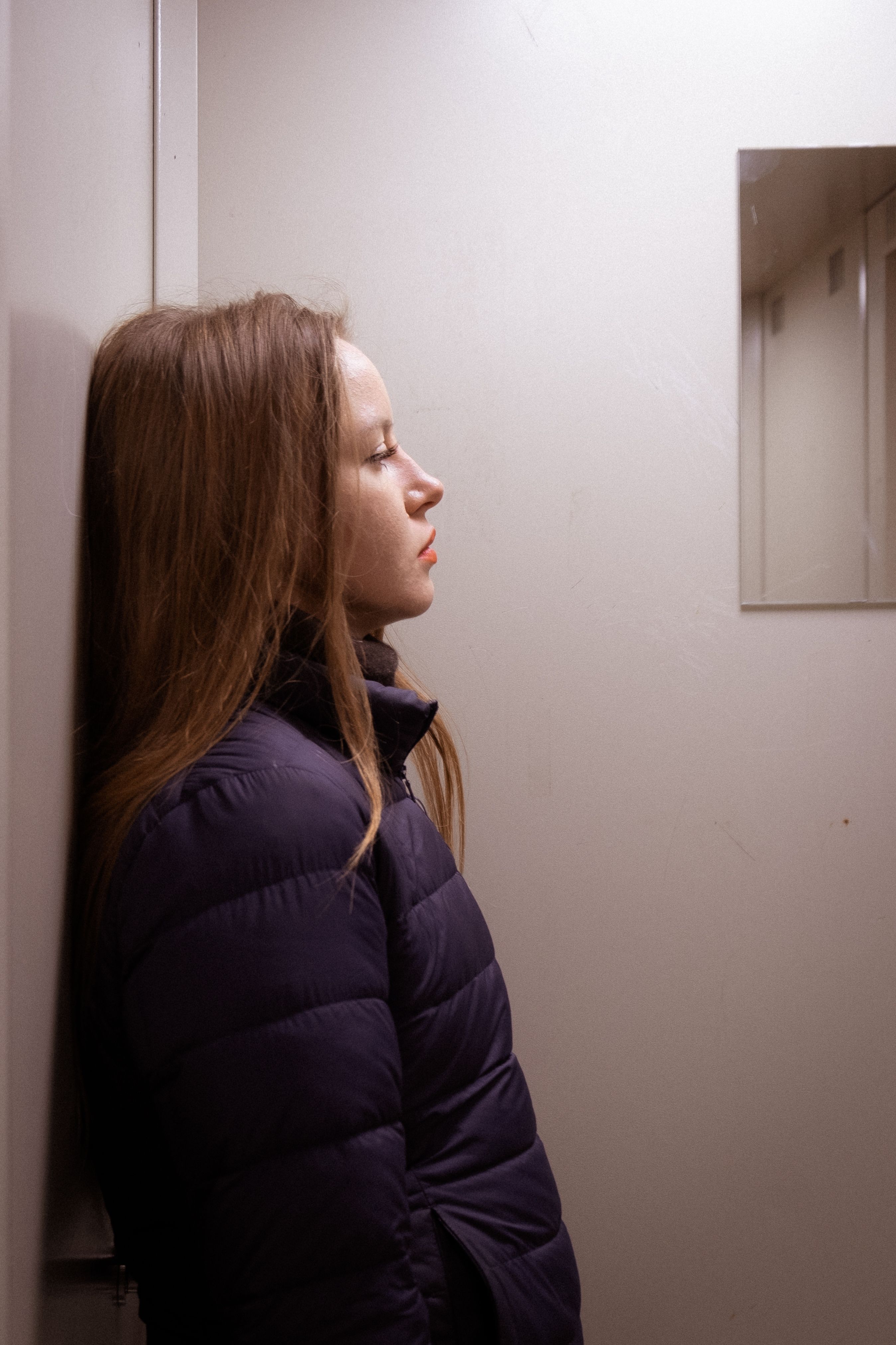 Side profile of an adult woman in a jacket leaning against a wall.