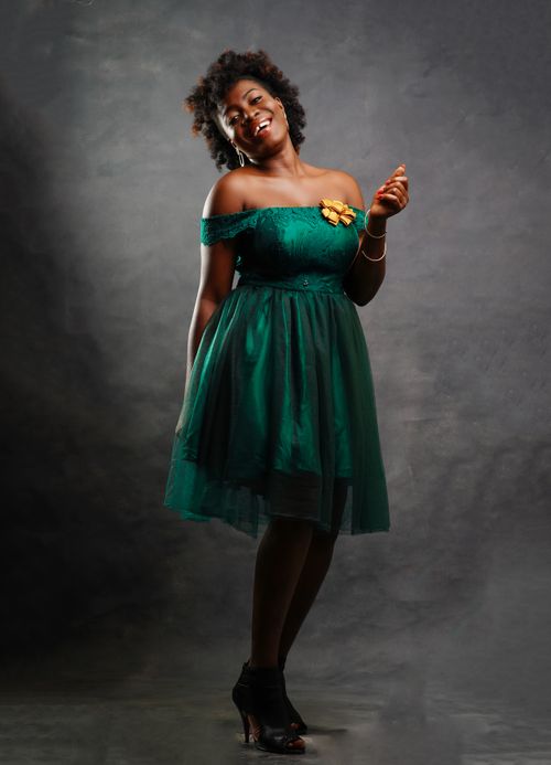 Free Charming African American woman in green dress smiling gracefully in a studio setting. Stock Photo