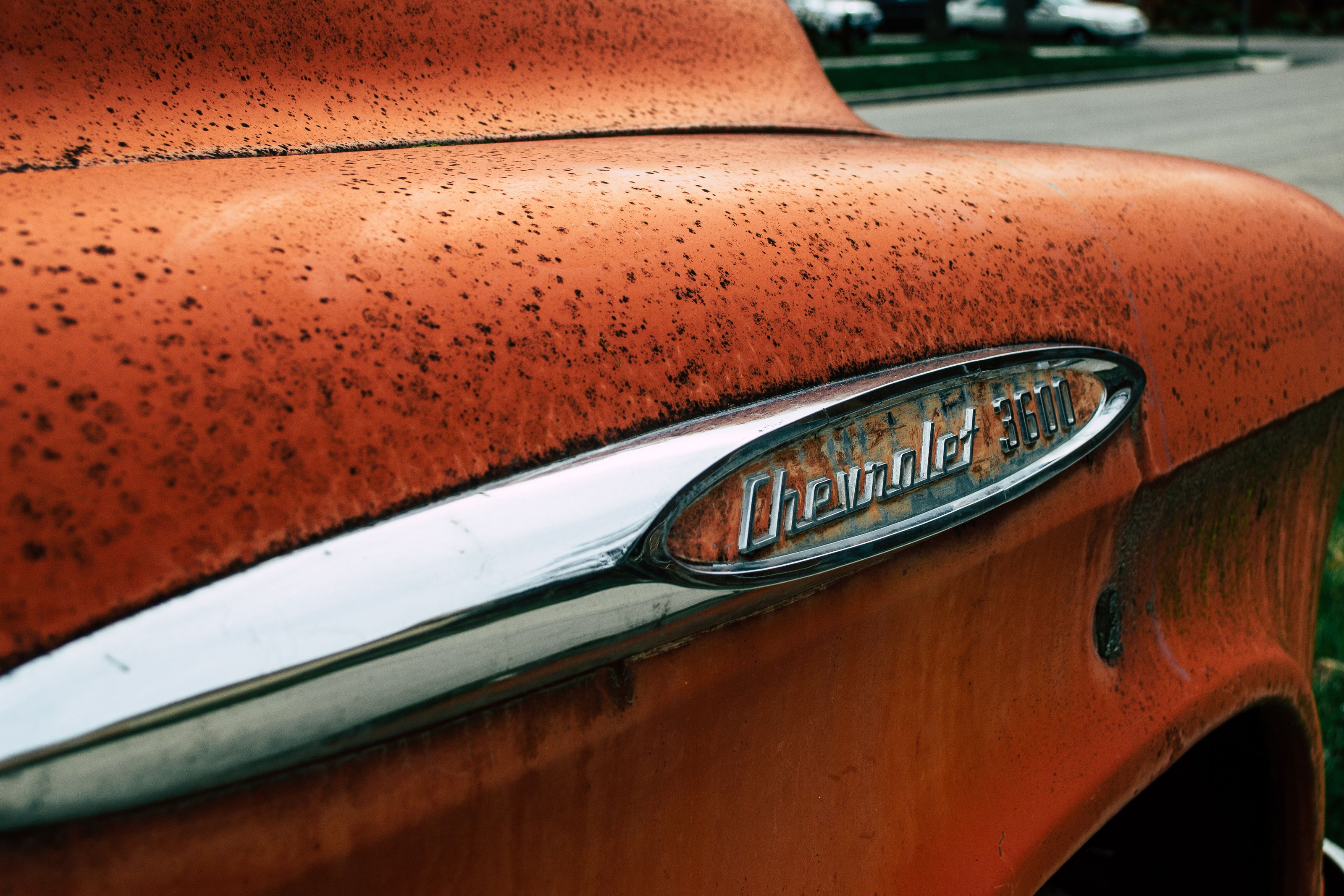 Close-up of a vintage Chevrolet 3600 emblem on a rusty orange truck outdoors.