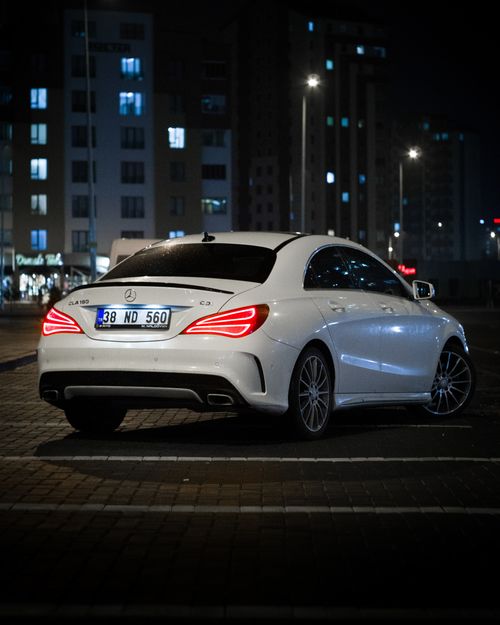 Free White Mercedes Benz CLA parked in an urban setting at night with illuminated buildings in the background. Stock Photo