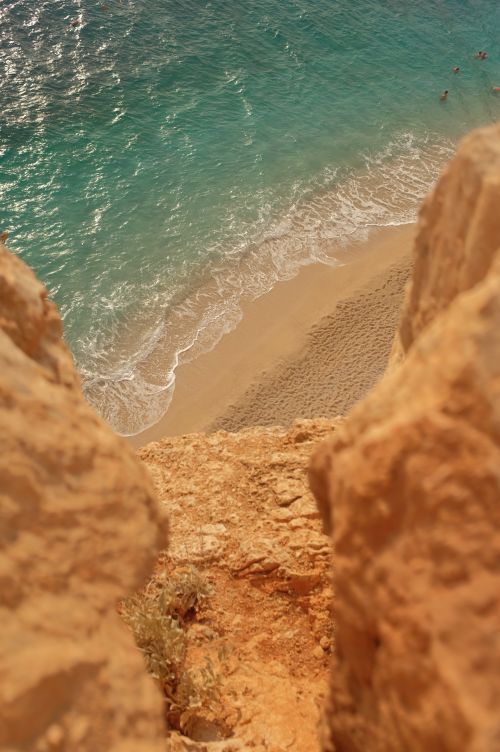 Free Dramatic coastal cliff overlooking a sandy beach and turquoise ocean, perfect for travel and nature themes. Stock Photo