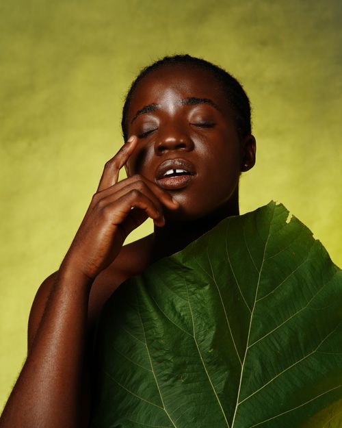 Free Portrait of a woman with eyes closed, draped in a green leaf against a yellow backdrop. Stock Photo