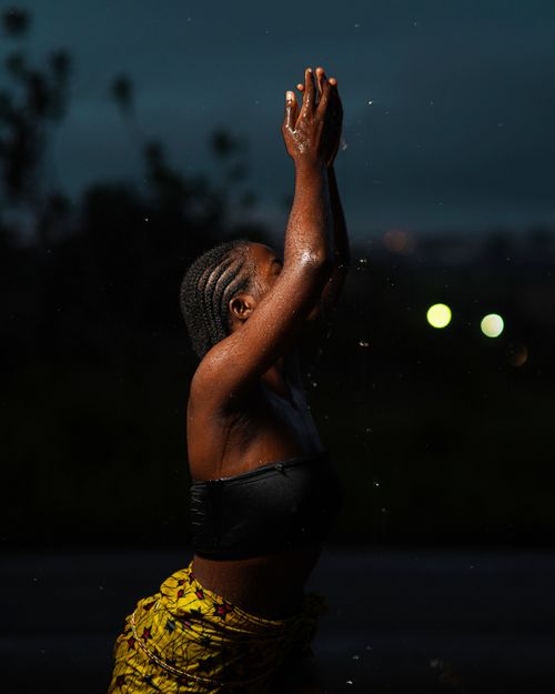 Free A woman with braided hair raises her hands at night, creating a striking silhouette. Stock Photo
