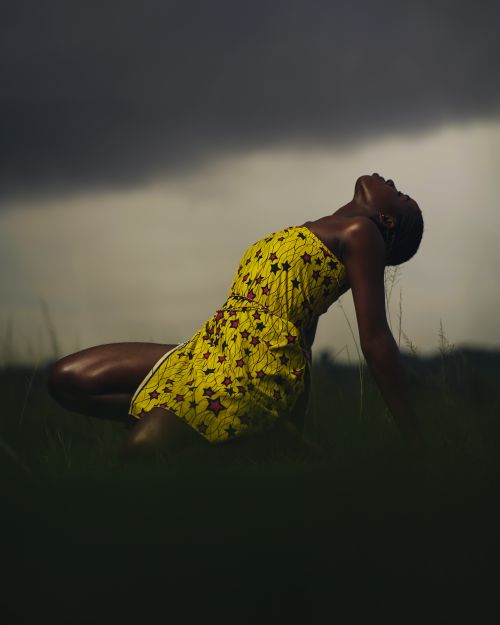Free Artistic shot of a woman posing outdoors in a vibrant yellow dress with a cloudy background. Stock Photo