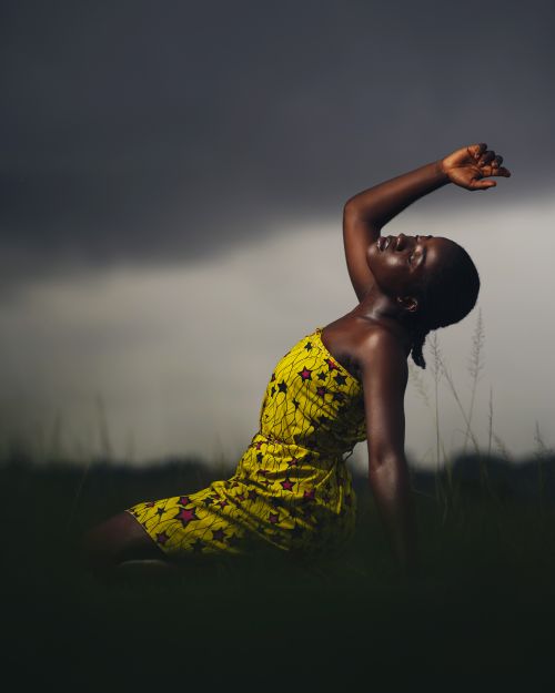 Free An African American woman poses gracefully in a yellow dress against a moody sky. Stock Photo
