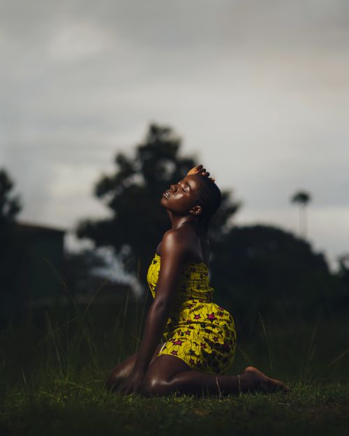Free A beautiful woman wearing a yellow dress poses gracefully in nature during twilight. Stock Photo