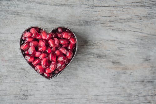бесплатная Чаша с серебряным сердечком, наполненная семенами красного граната Стоковое фото