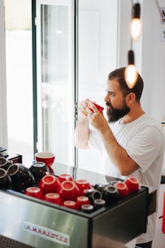 A bearded man in a cafe savoring a cup of coffee, looking out the window.
