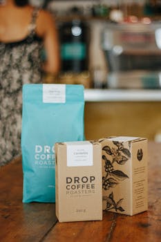 High-quality coffee packaging displayed on a wooden tabletop in a cozy café environment.