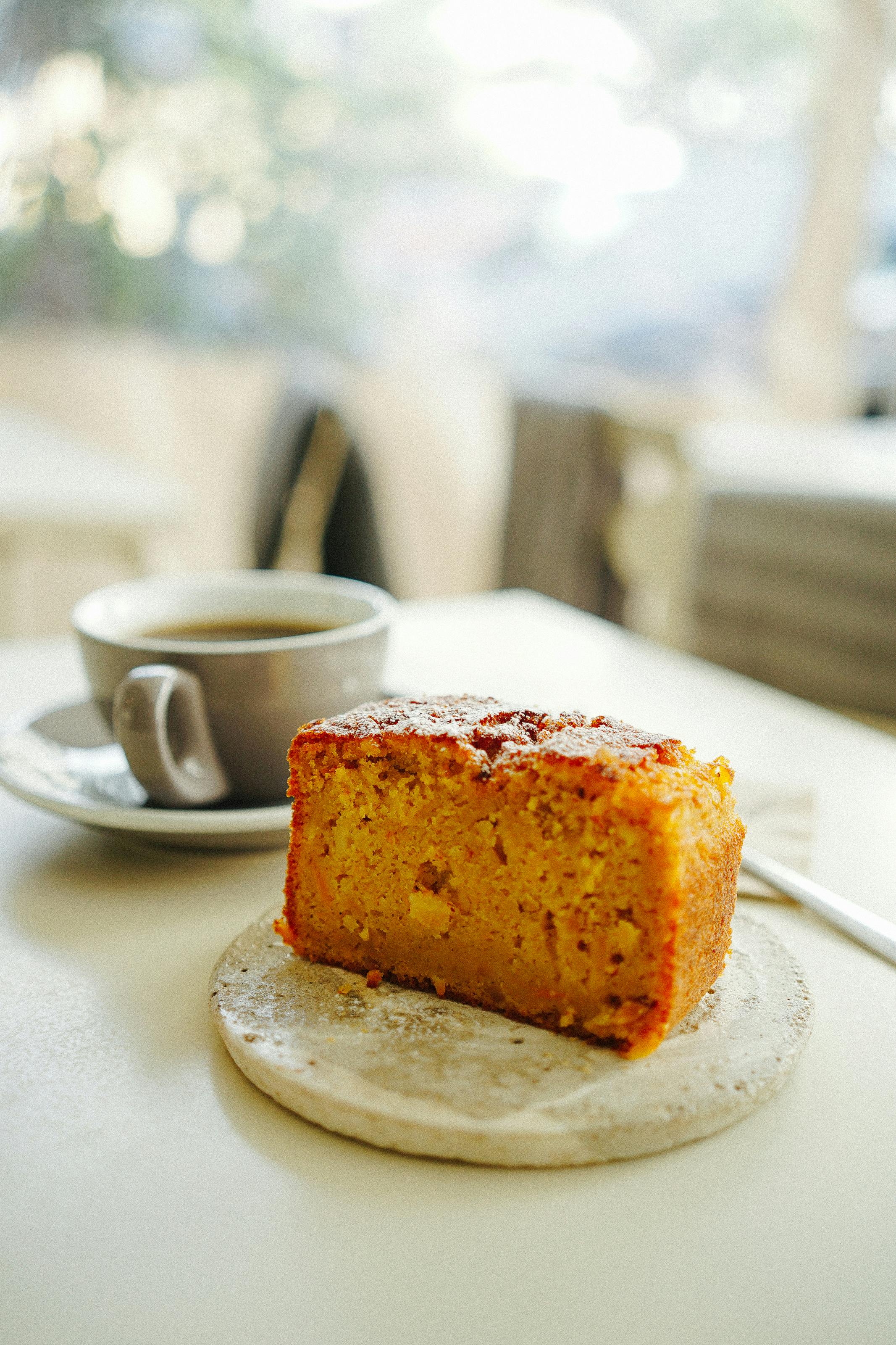 A slice of fresh cake and a coffee cup on a table in a cozy café setting.