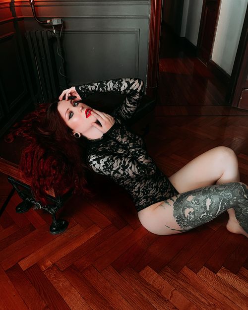 Free Red-haired woman in lace bodysuit posing sensually indoors on wooden flooring. Stock Photo