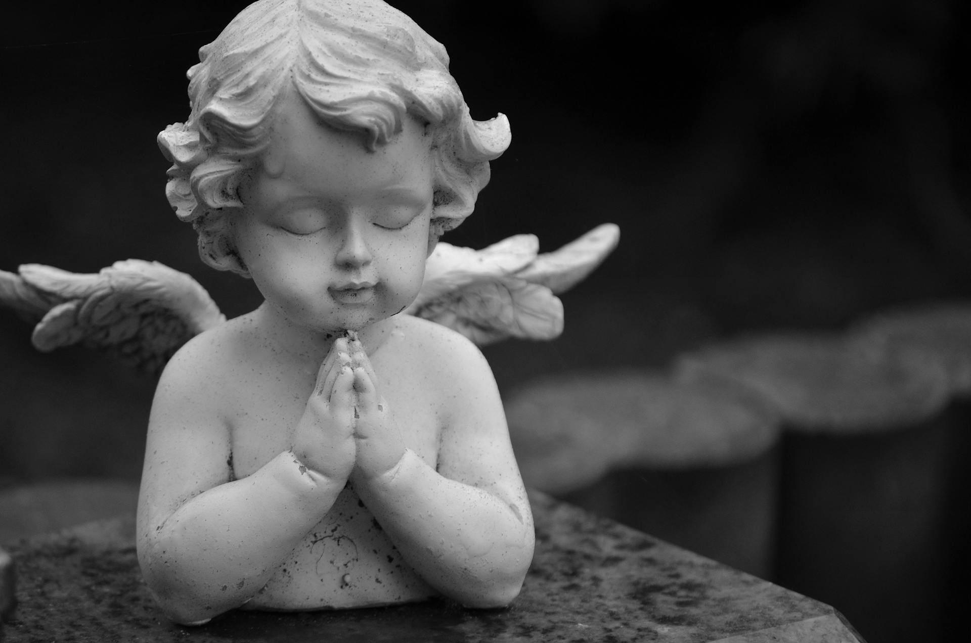 A Grayscale of a Praying Baby Angel Figurine