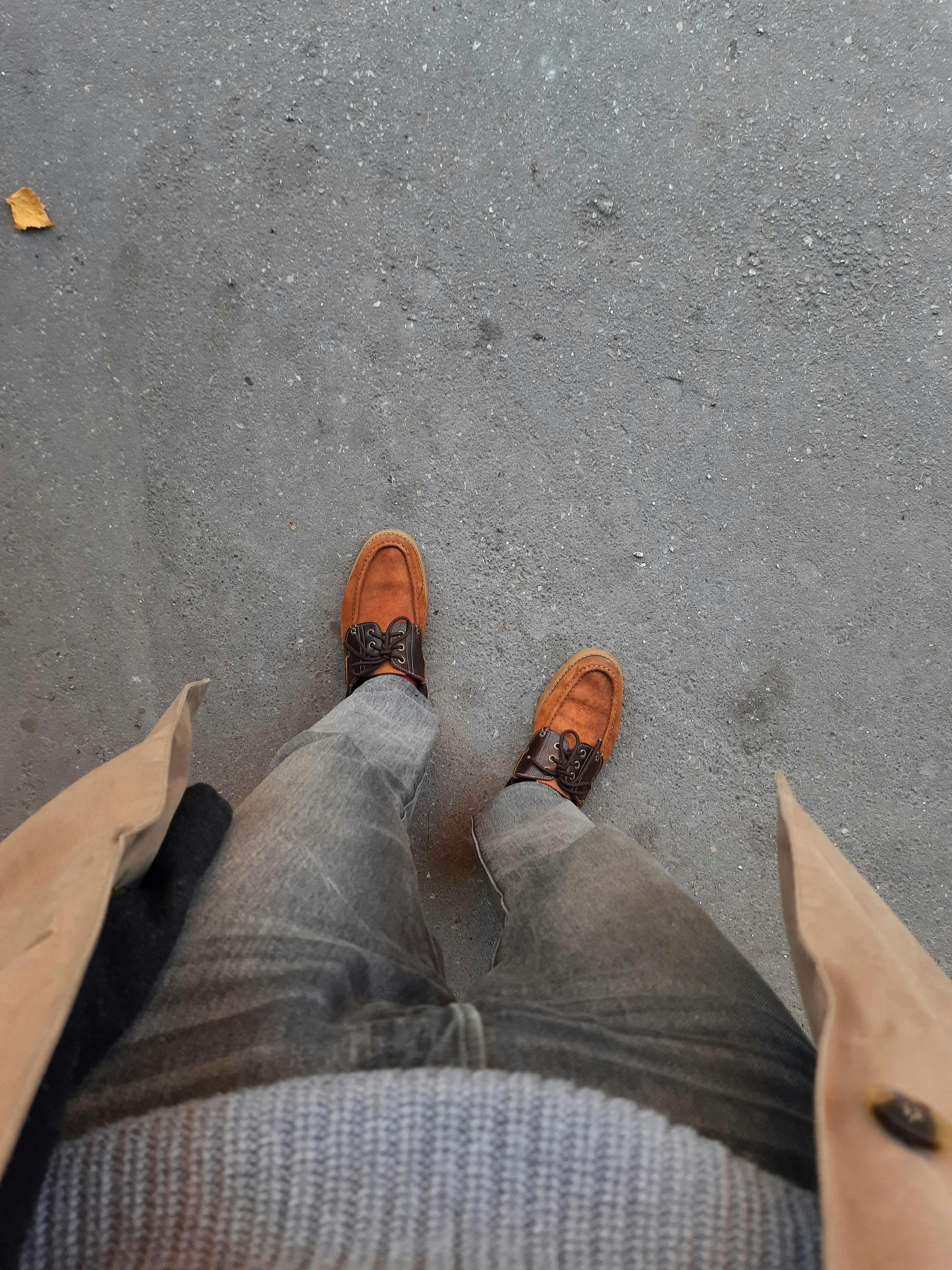 A top-down view of a casual outfit with brown leather shoes and denim jeans on a textured ground.