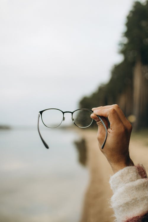 Free Selective Focus Photo of a Person's Hand Holding Black Framed Eyeglasses Stock Photo