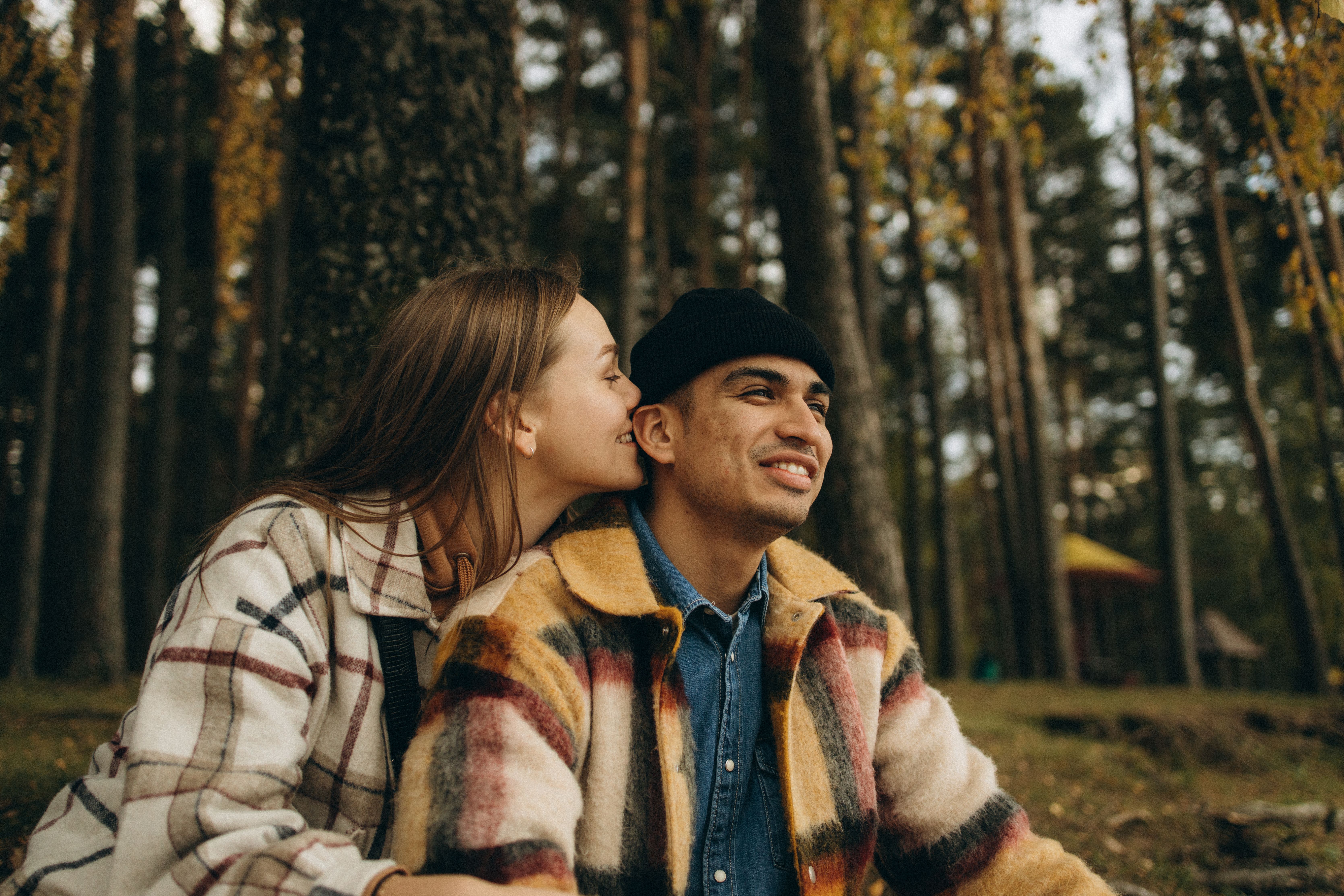 A young couple shares a tender moment in a serene autumn forest setting.
