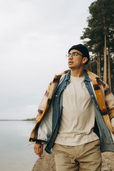Young man in layered clothing strolling along a serene beach surrounded by nature.