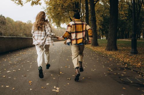 Free A couple joyfully runs hand in hand down a tree-lined street during autumn. Stock Photo