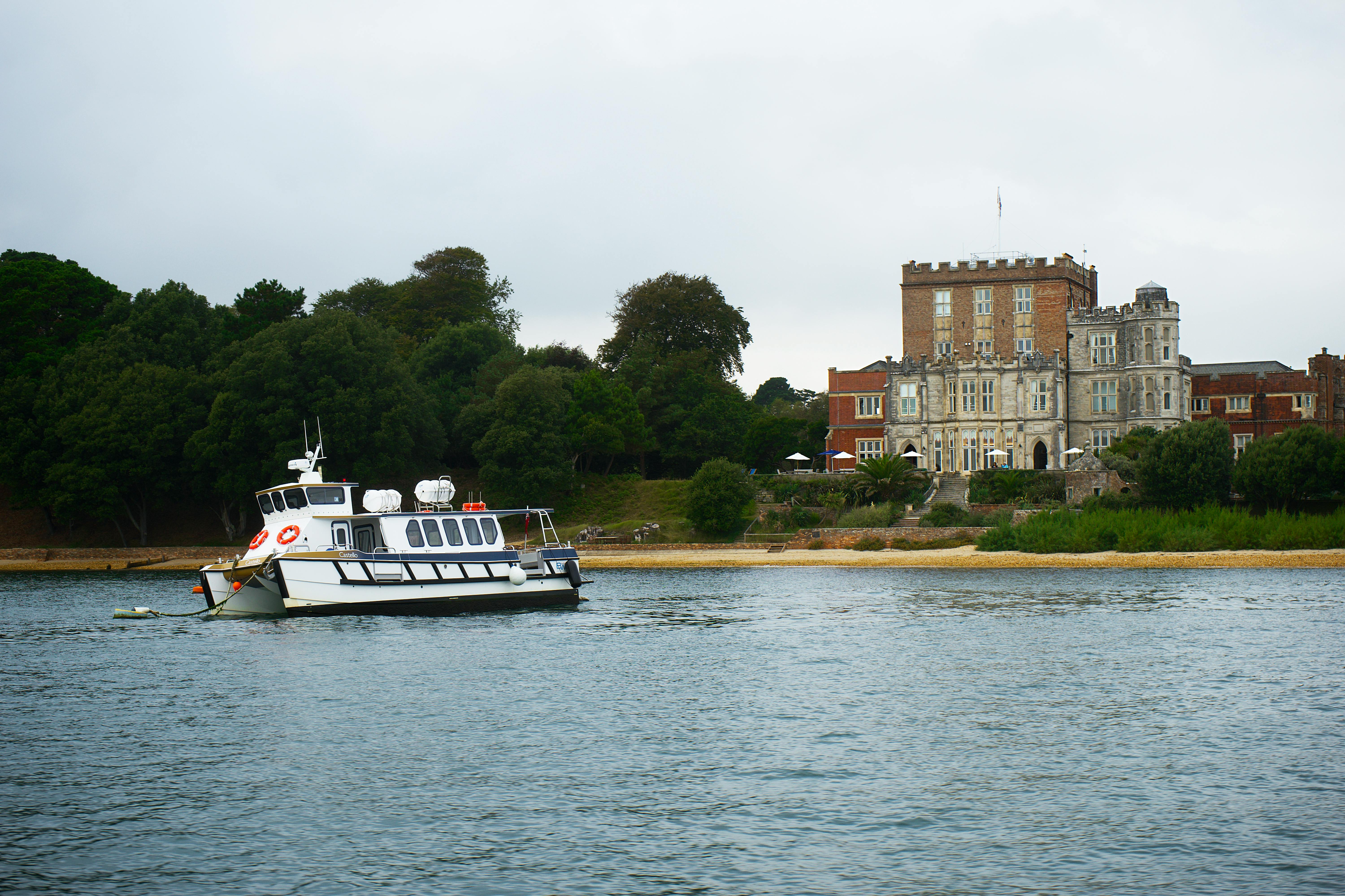 A peaceful scene of a boat near a historic castle in Poole, England, surrounded by lush greenery and calm waters.