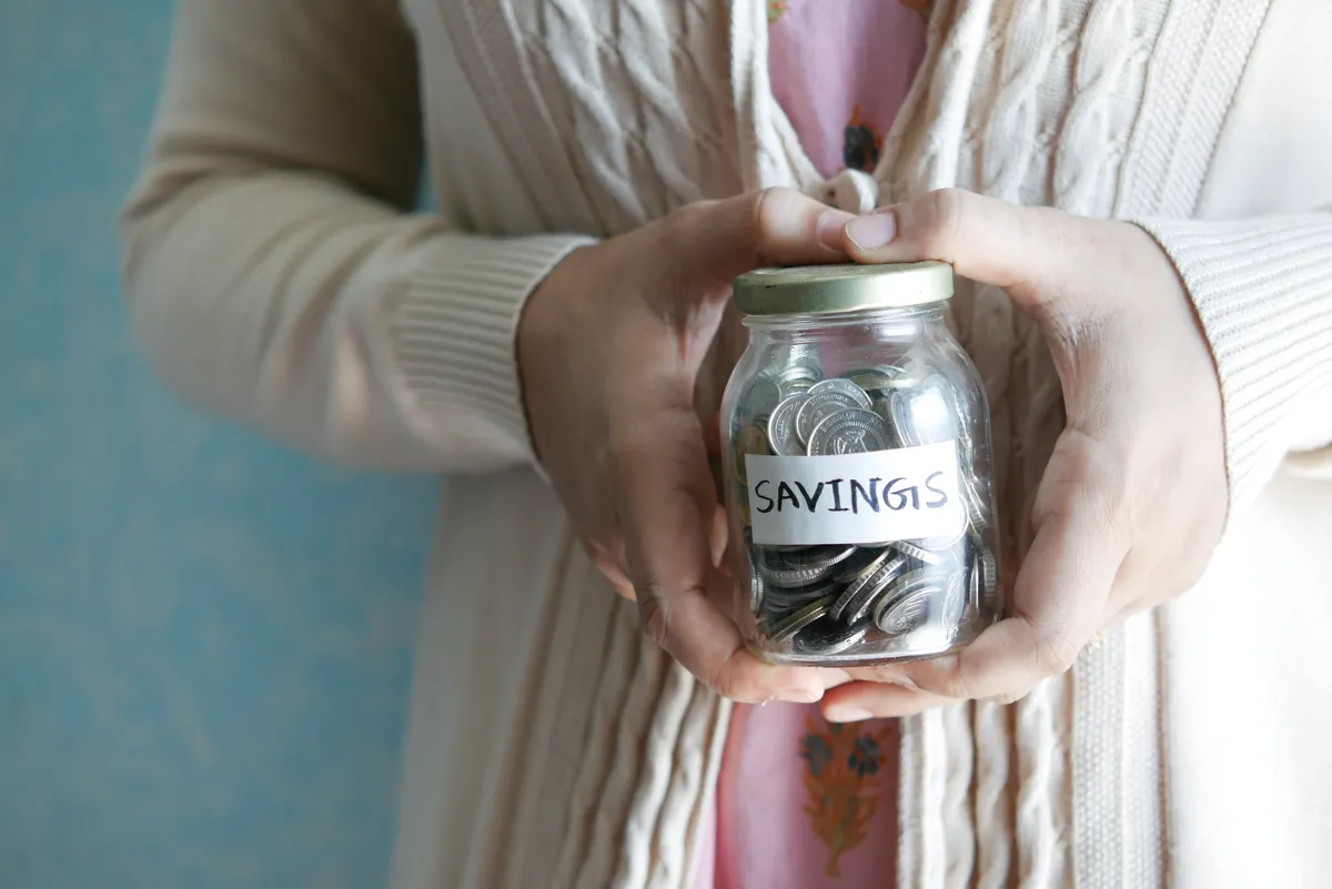 Wanita memegang toples savings berisi koin sebagai simbol tujuan finansial jangka panjang
