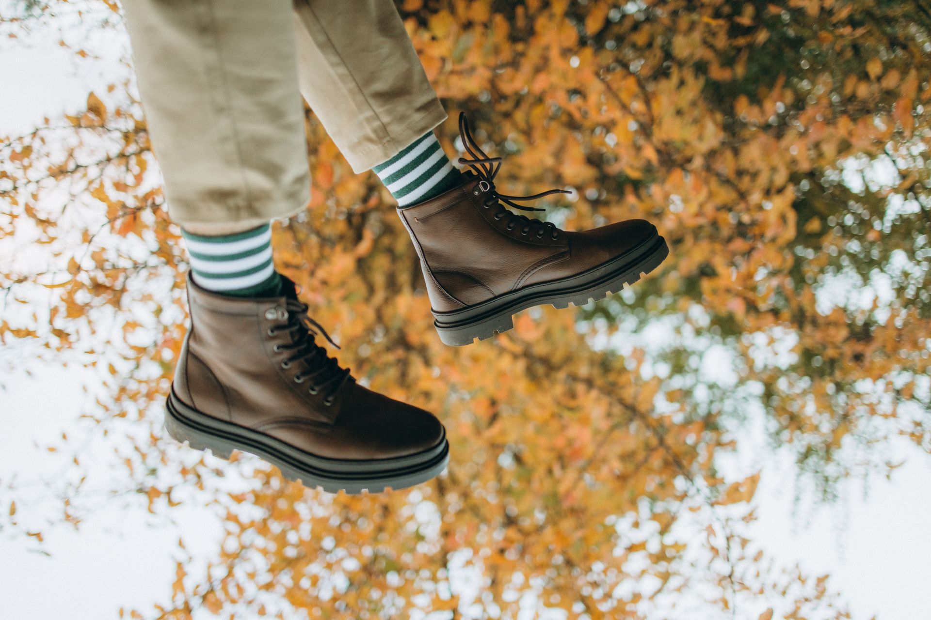 Close-up of leather boots and striped socks against a backdrop of autumn leaves.