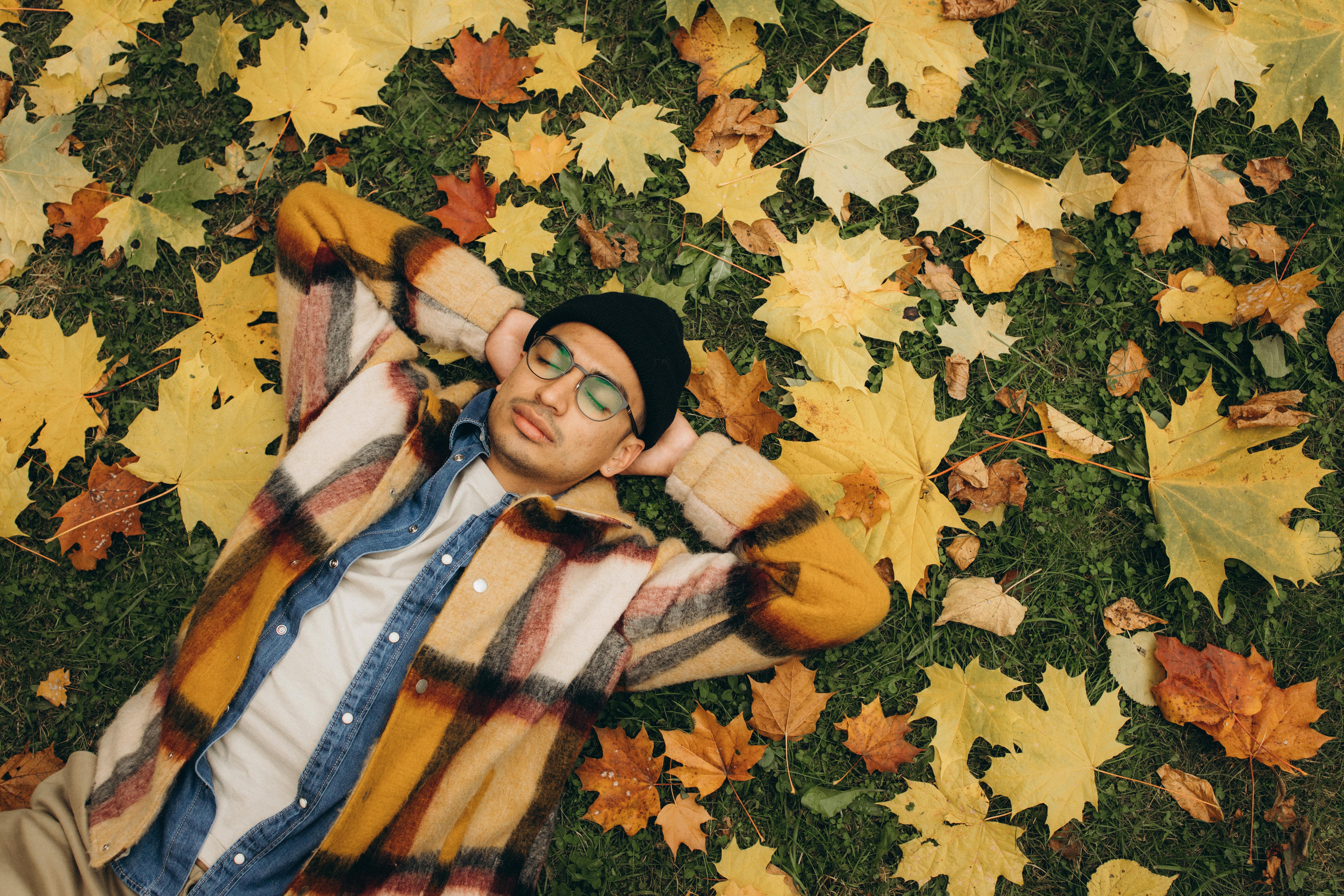 Man lying on autumn leaves with a plaid coat, showcasing a peaceful fall moment.