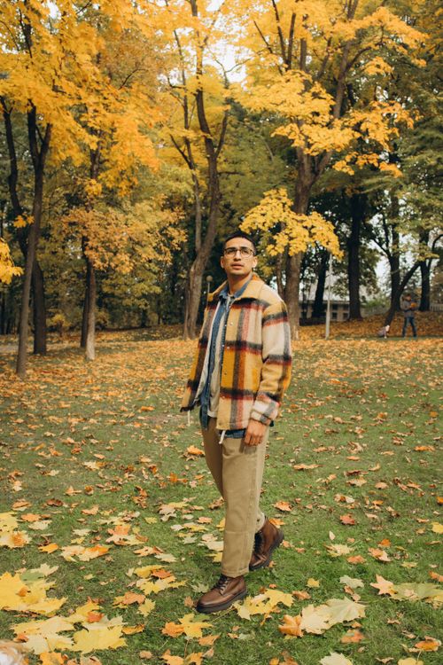 Free An Asian man stands in a park filled with colorful autumn foliage, wearing a warm checkered jacket. Stock Photo