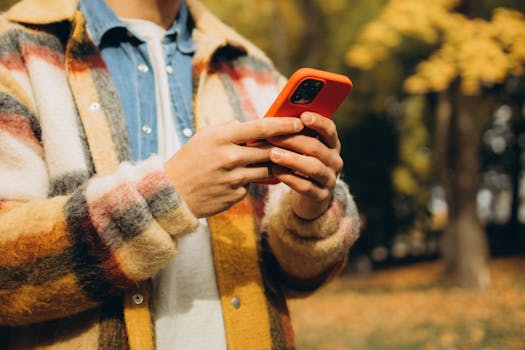 Person in checkered jacket using smartphone outside during autumn day.